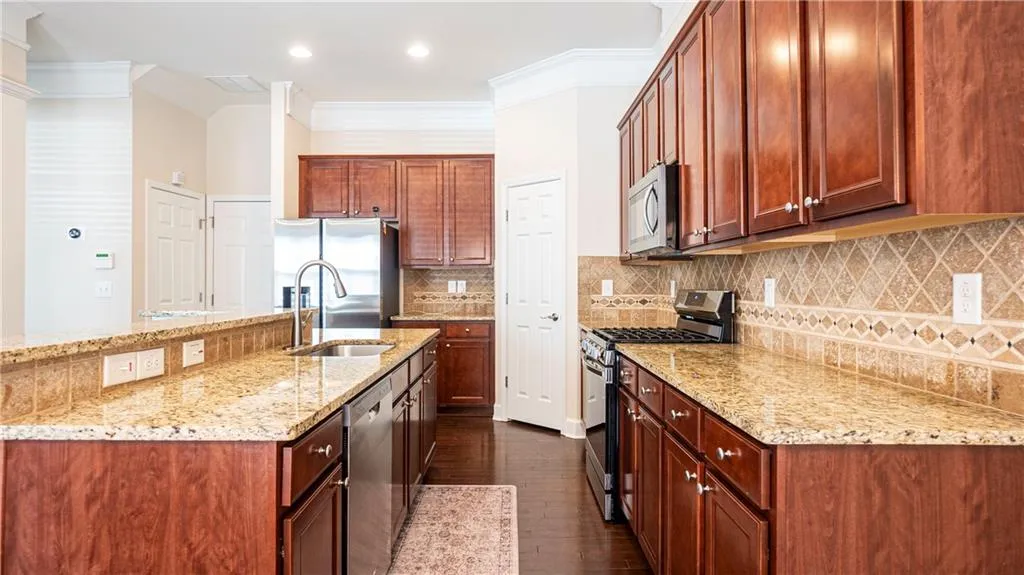 Kitchen with stainless steel appliances, light stone counters, dark wood-style flooring, a kitchen island with sink, and crown molding
