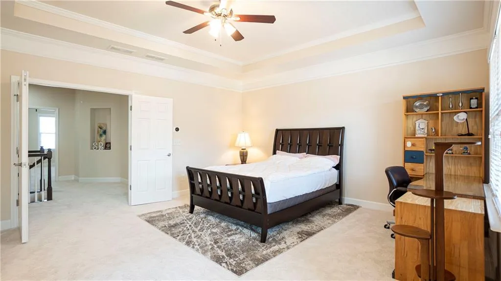 Bedroom featuring light carpet, crown molding, a tray ceiling, and a ceiling fan