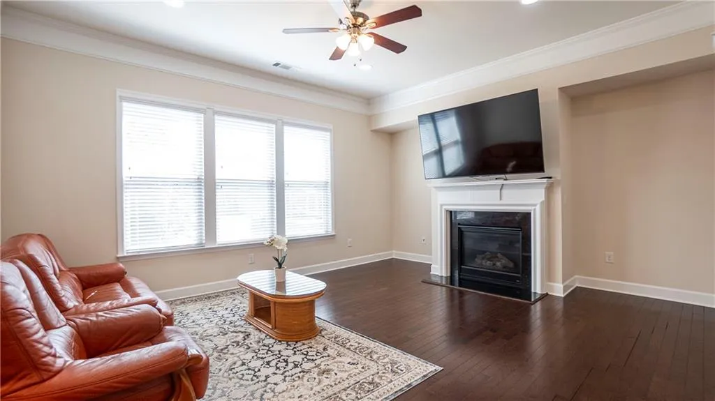 Living room featuring a ceiling fan, dark wood-style flooring, ornamental molding, and a glass covered fireplace