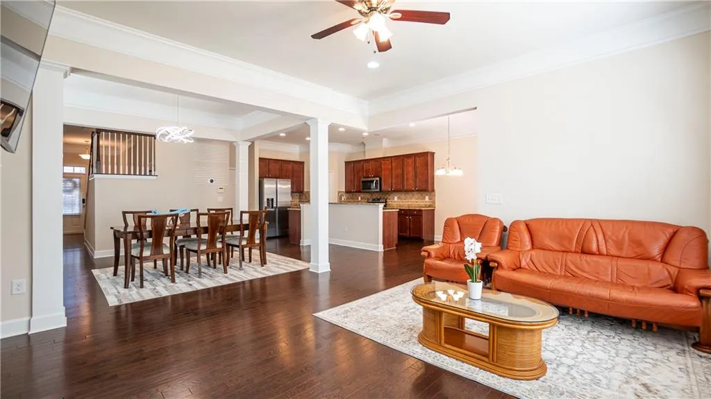 Living room with a chandelier, dark wood-style flooring, ceiling fan, ornate columns, and ornamental molding