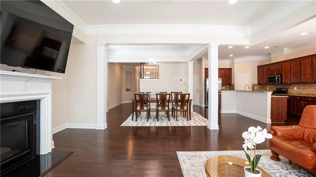 Living room with dark wood-style floors, ornate columns, ornamental molding, a fireplace, and hanging lights