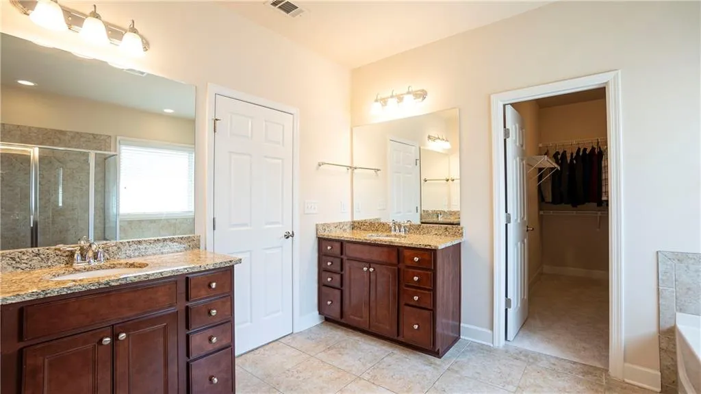 Bathroom featuring two vanities, a shower stall, light tile patterned floors, a spacious closet, and a bath