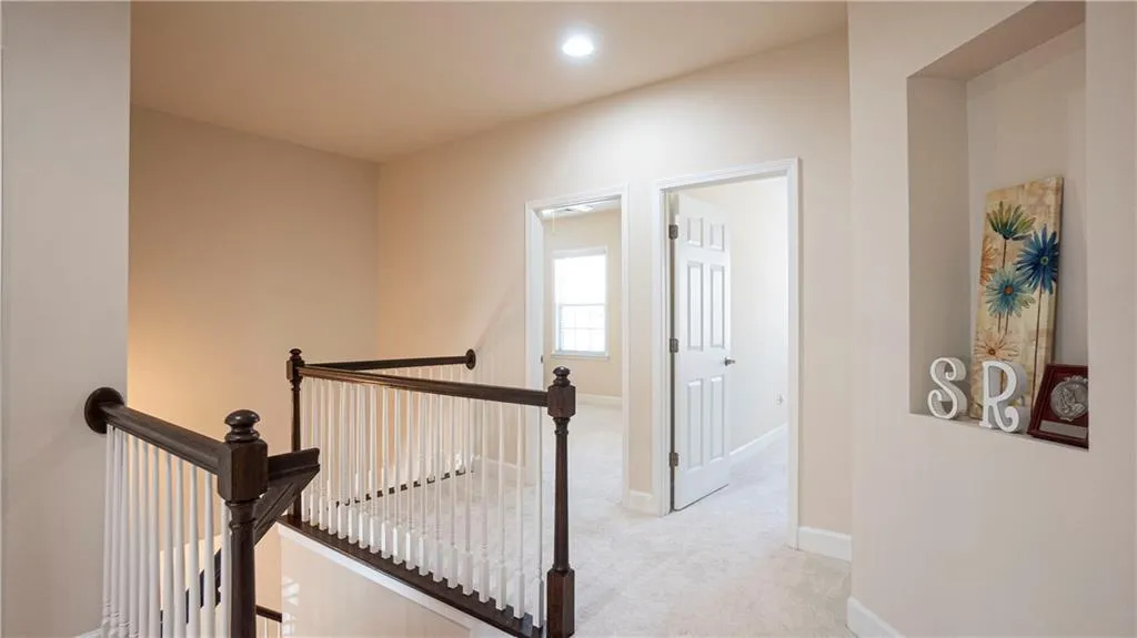 Hall with an upstairs landing, light colored carpet, and recessed lighting