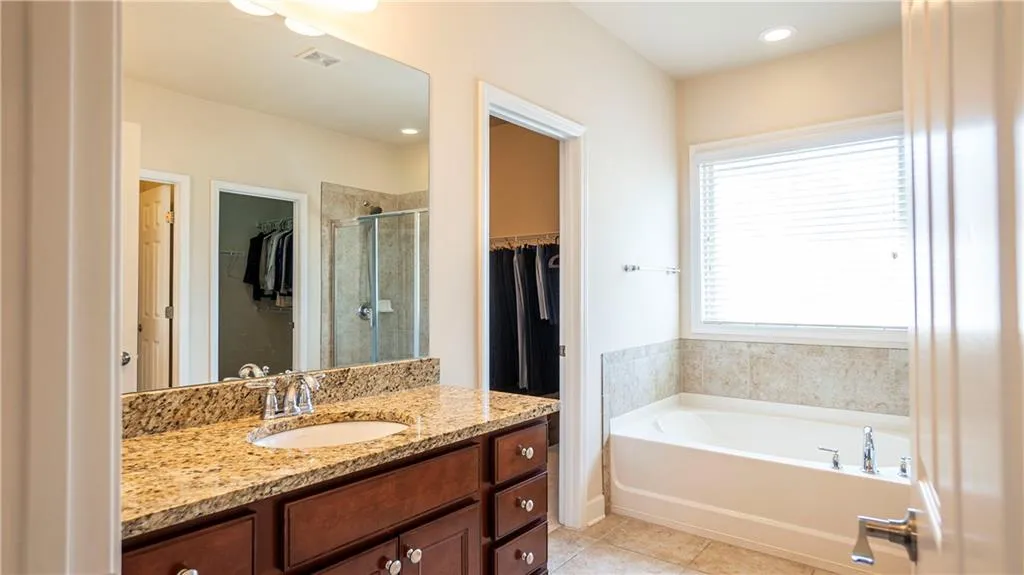 Full bathroom with a walk in closet, vanity, a stall shower, a garden tub, and light tile patterned floors