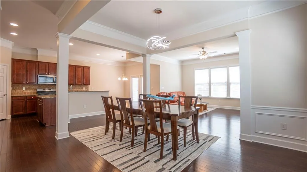 Dining area featuring decorative columns, hanging lights, dark wood-type flooring, ceiling fan, and ornamental molding
