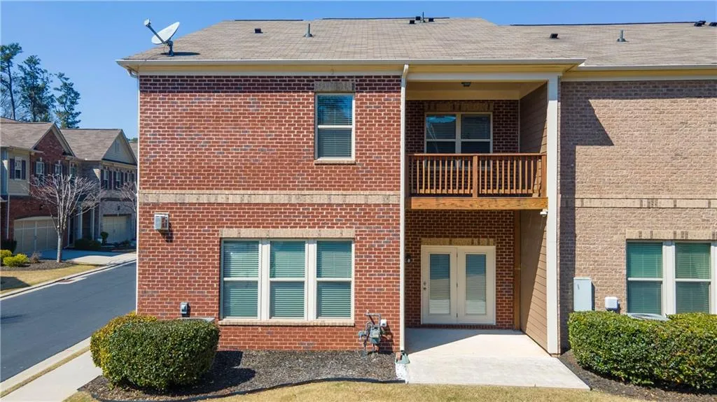 Back of property with brick siding, a balcony, a shingled roof, and a patio area