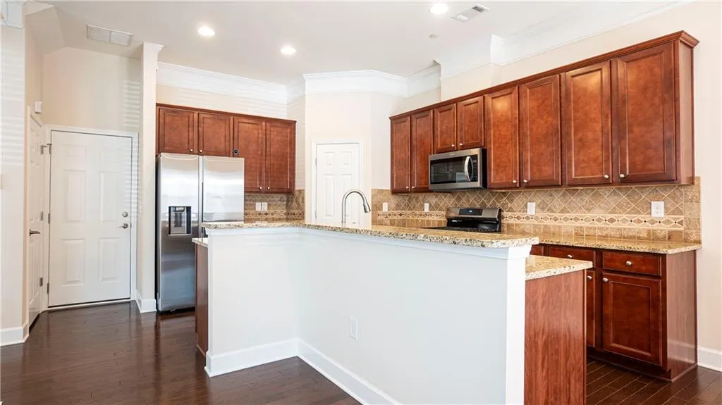 Kitchen featuring a kitchen island with sink, stainless steel appliances, dark wood-style flooring, tasteful backsplash, and ornamental molding