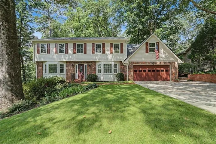 Traditional home featuring a two-car garage with a wood-finish door, brick accenting, and bay window