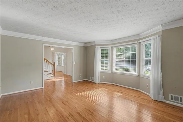 Hardwood flooring throughout a spacious room with a bay window and crown molding