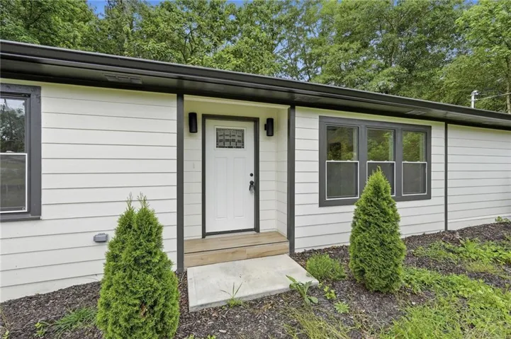 Contemporary exterior featuring white horizontal siding with dark trim, a white front door with decorative glass, black wall sconces, a wood-finish porch step, and a concrete landing