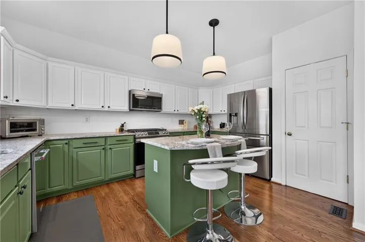 Kitchen featuring two-tone cabinetry with white upper and green lower cabinets, stainless steel appliances, and wood-finish flooring