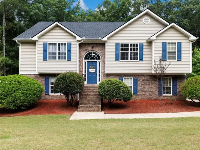 Split-level residence featuring a brick and siding exterior, a dark shingle roof, and a prominent arched entryway with a blue door