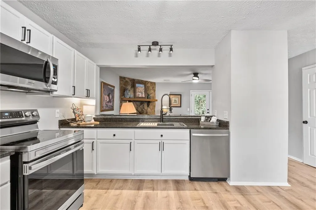 Kitchen featuring appliances with stainless steel finishes, white cabinetry, light wood-style flooring, dark stone counters, and a textured ceiling