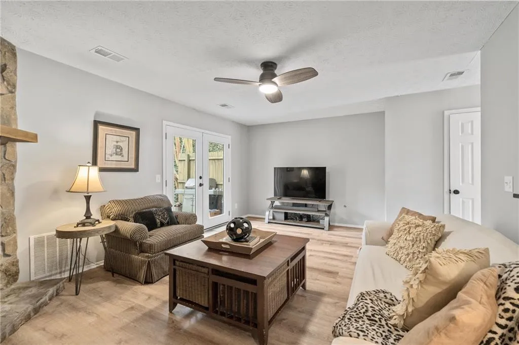 Living room featuring light wood-type flooring, ceiling fan, a textured ceiling, and french doors