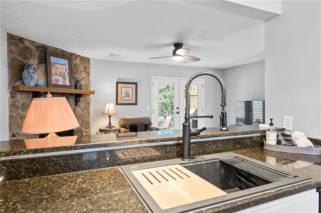 Kitchen with open floor plan, a textured ceiling, a stone fireplace, and a ceiling fan