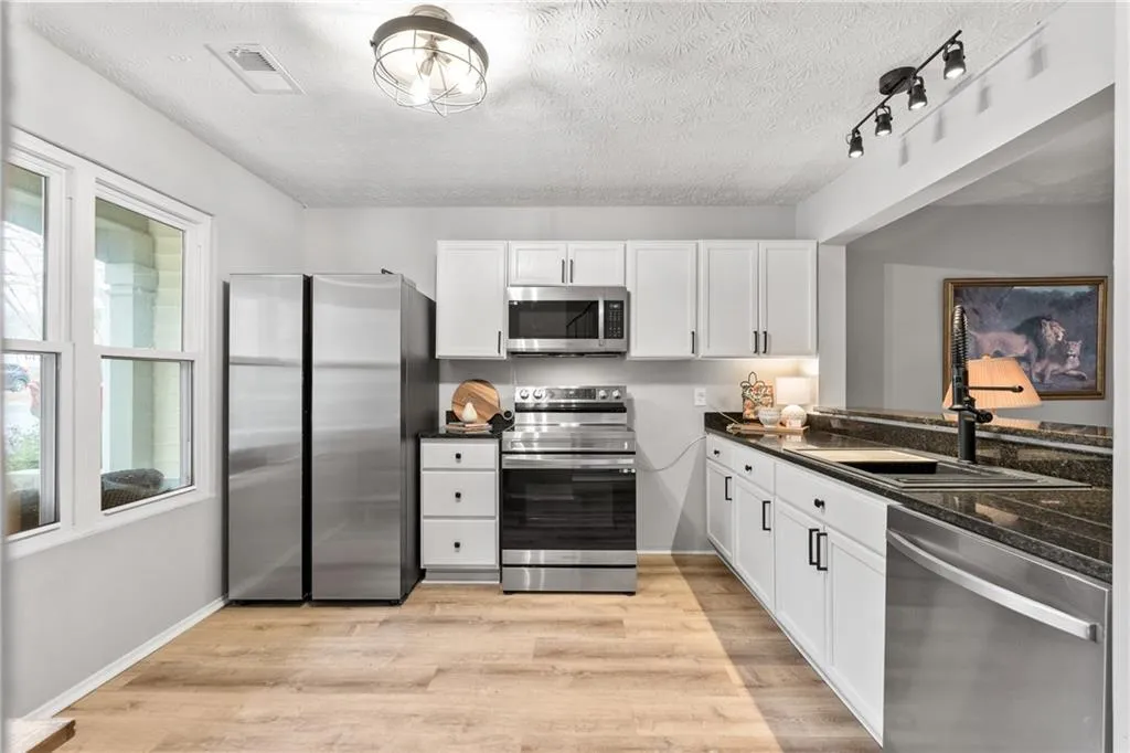 Kitchen featuring appliances with stainless steel finishes, white cabinets, dark stone countertops, light wood-style flooring, and a textured ceiling