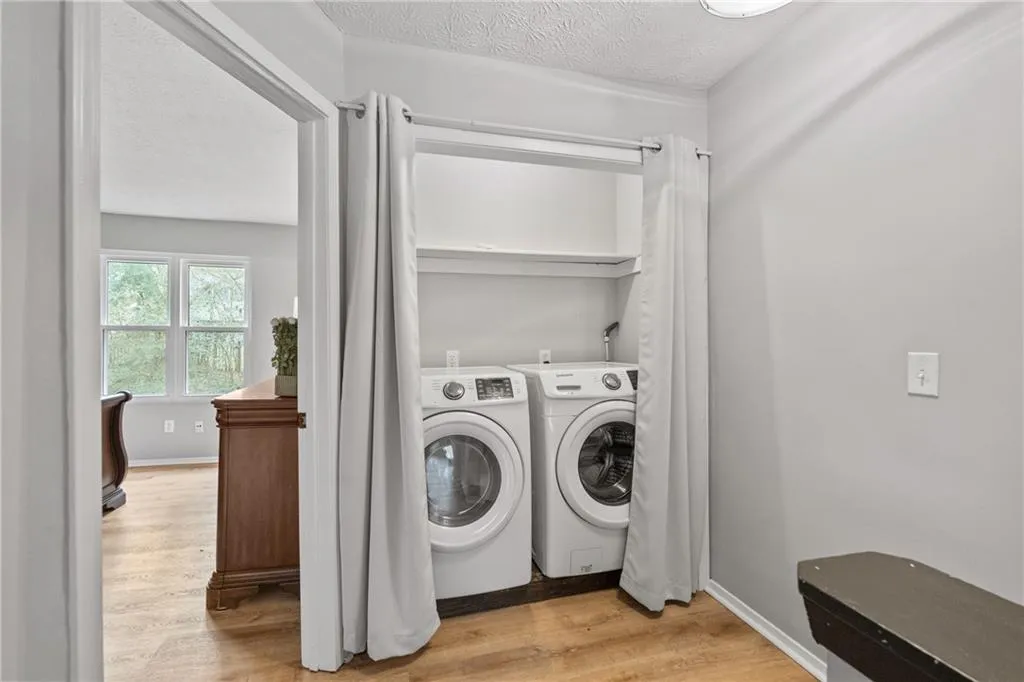 Laundry area with light wood-style floors, a textured ceiling, and washing machine and clothes dryer