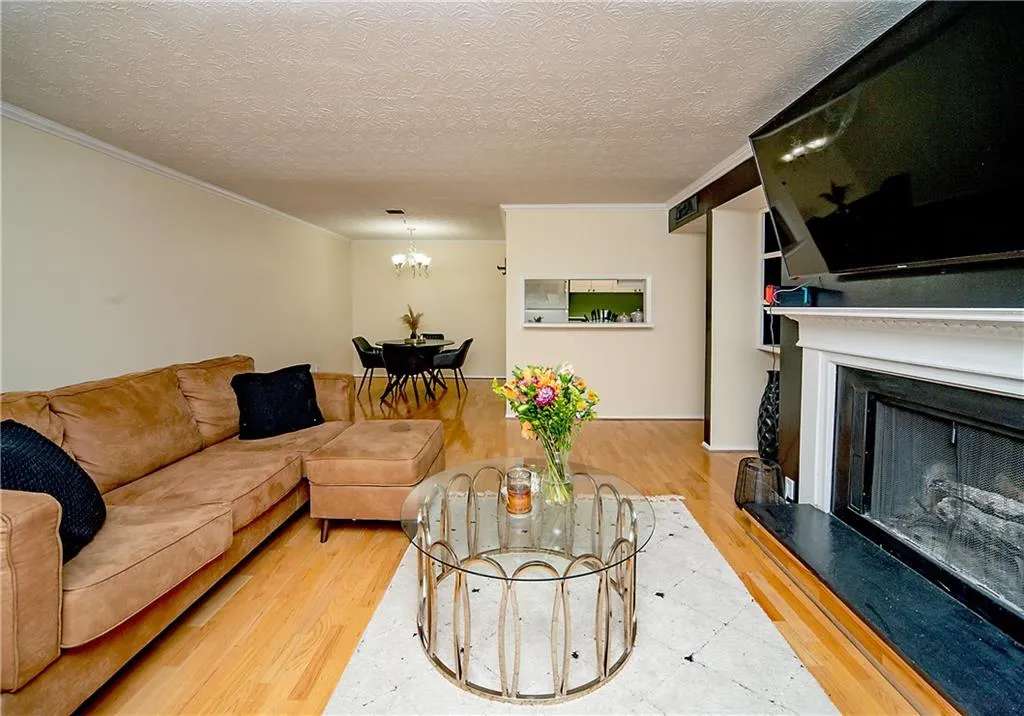 Living area featuring wood finished floors, a fireplace with raised hearth, a chandelier, a textured ceiling, and crown molding