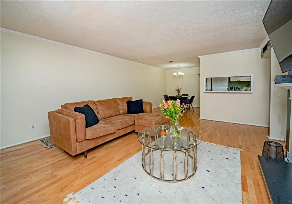 Living room featuring ornamental molding, a chandelier, wood finished floors, baseboards, and a textured ceiling