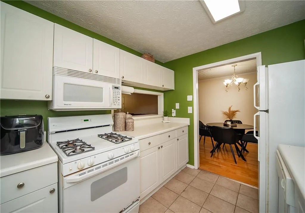 Kitchen featuring white appliances, a chandelier, light tile patterned floors, white cabinetry, and a textured ceiling