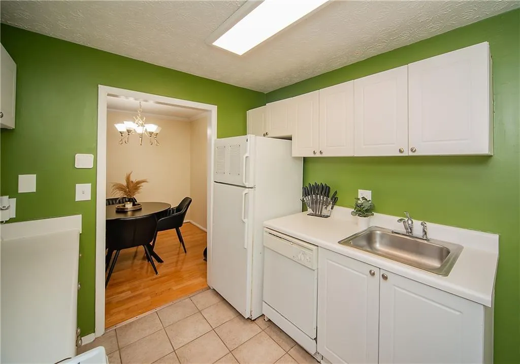 Kitchen with white appliances, a sink, white cabinets, light countertops, and light tile patterned floors