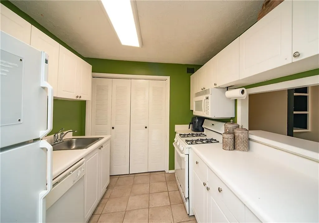 Kitchen with white appliances, a sink, white cabinets, and light countertops
