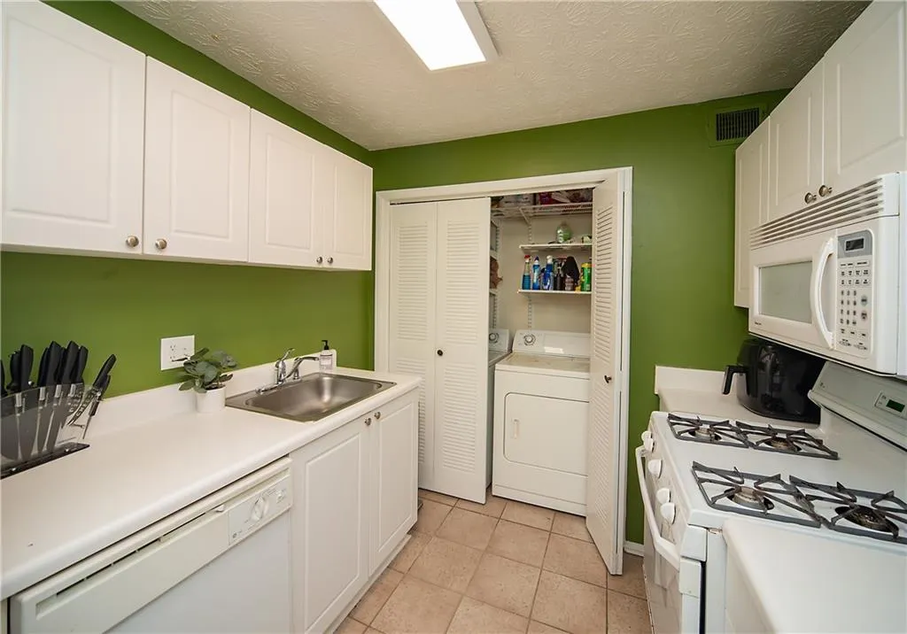 Kitchen featuring white appliances, a sink, white cabinets, light countertops, and light tile patterned flooring