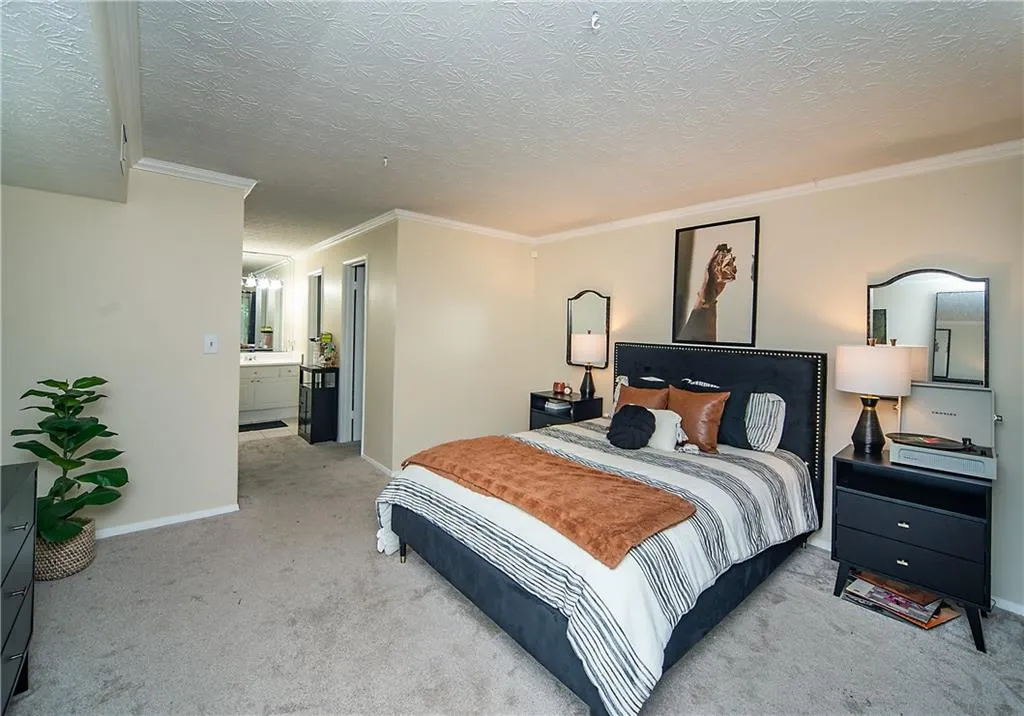 Bedroom featuring light colored carpet, ornamental molding, baseboards, a textured ceiling, and a chandelier