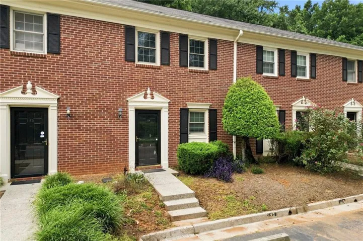 Brick exterior featuring white window frames with black shutters, decorative door surrounds, and concrete walkways