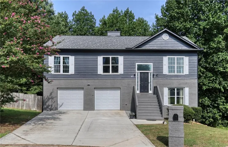 Multi-level residence featuring a two-car garage, prominent front entry stairs, white window shutters, and a shingled roof