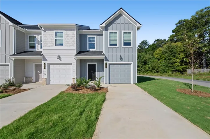 Modern townhome exterior featuring board and batten siding, shaker shingle accents, attached garage, and a private driveway