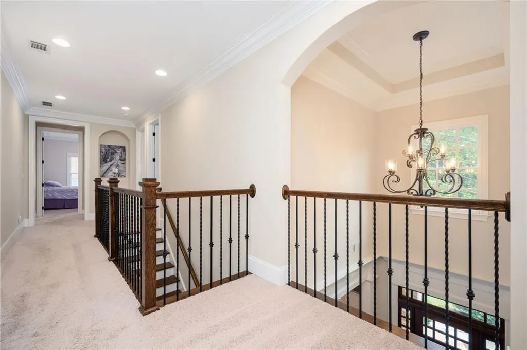 Hall featuring an upstairs landing with arched views of   chandelier in 2 story foyer