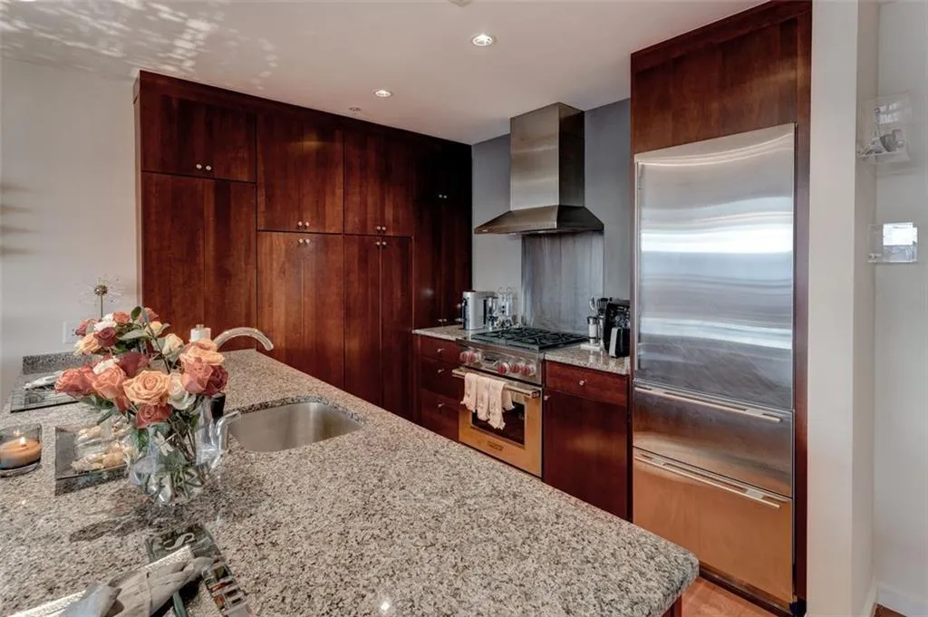 Kitchen with wall chimney range hood, a kitchen island with sink, light stone countertops, and high end appliances Kitchen with wall chimney range hood, a kitchen island with sink, light stone countertops, and high end appliances