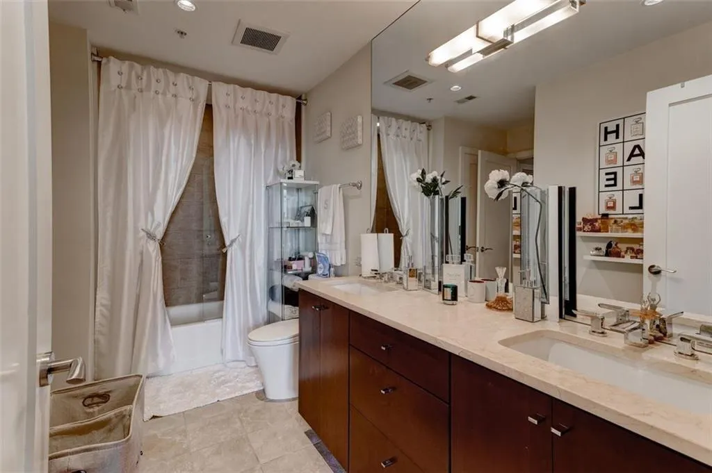 Full bathroom with double sink, shower / bath combination with curtain, tile flooring, toilet, and vanity with extensive cabinet space Full bathroom with double sink, shower / bath combination with curtain, tile flooring, toilet, and vanity with extensive cabinet space