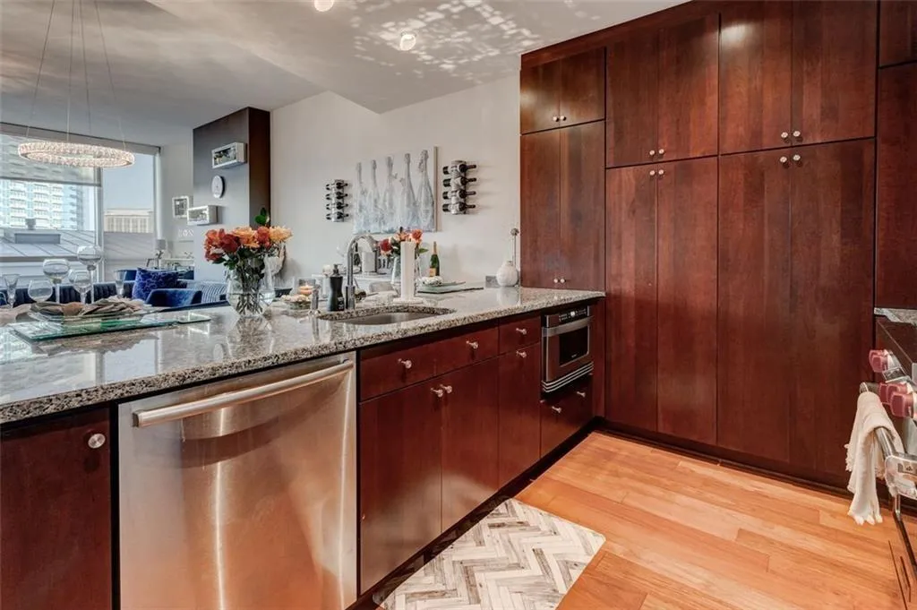 Kitchen with sink, light stone counters, light hardwood / wood-style flooring, stainless steel dishwasher, and hanging light fixtures Kitchen with sink, light stone counters, light hardwood / wood-style flooring, stainless steel dishwasher, and hanging light fixtures