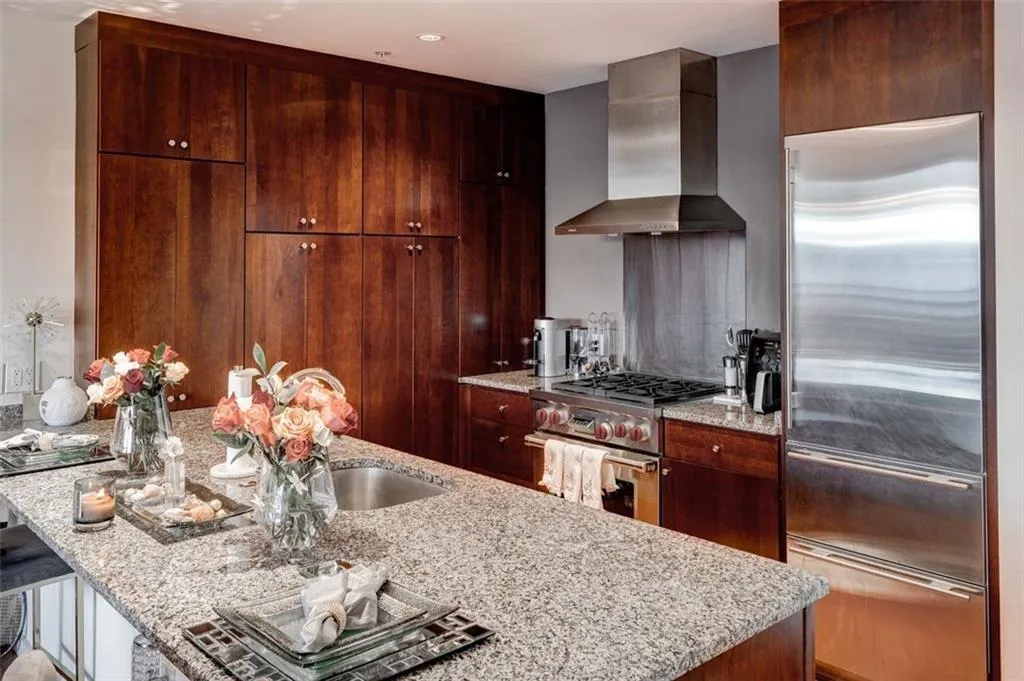 Kitchen with sink, light stone counters, wall chimney range hood, high quality appliances, and a kitchen bar Kitchen with sink, light stone counters, wall chimney range hood, high quality appliances, and a kitchen bar