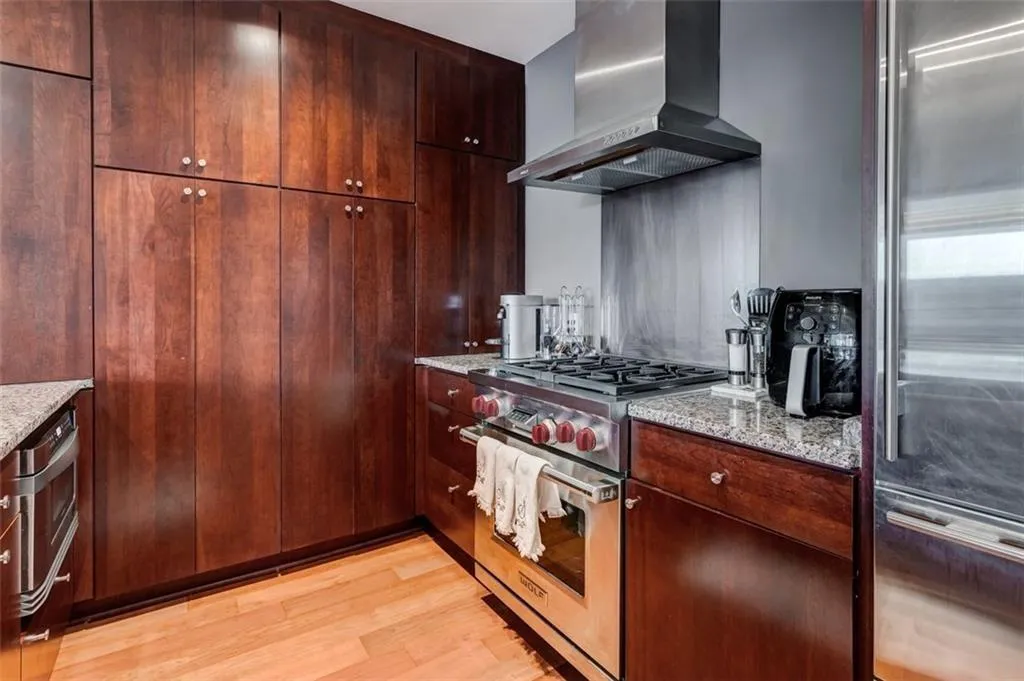 Kitchen with wall chimney exhaust hood, light stone counters, light hardwood / wood-style flooring, and high end appliances Kitchen with wall chimney exhaust hood, light stone counters, light hardwood / wood-style flooring, and high end appliances