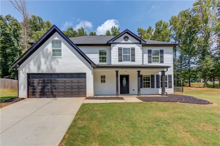 Two-story residence featuring a covered front porch, white siding, black shutters, and a two-car garage with a paved driveway
