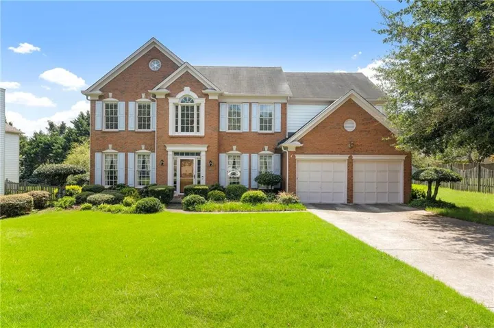 Brick exterior with white accents, a two-car garage, and a lush green lawn
