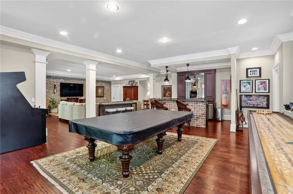 Rec room with decorative columns, crown molding, dark wood finished floors, recessed lighting, and brick wall