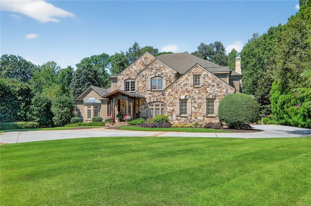 View of front facade with a front yard, a chimney, stone siding, and view of scattered trees