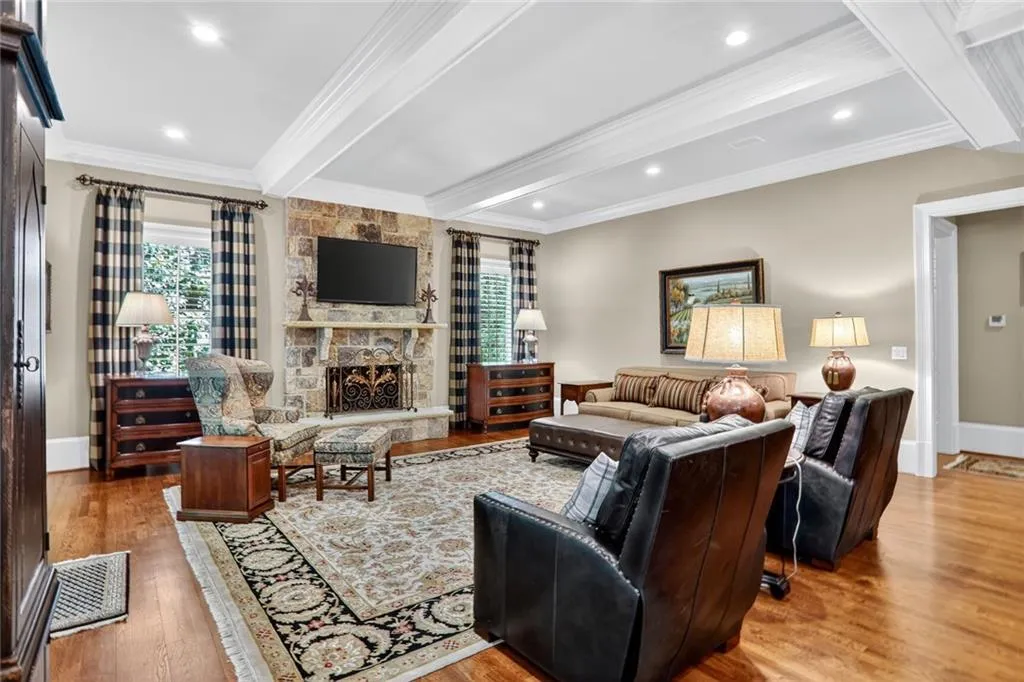 Living area with beam ceiling, light wood-style flooring, a stone fireplace, crown molding, and recessed lighting