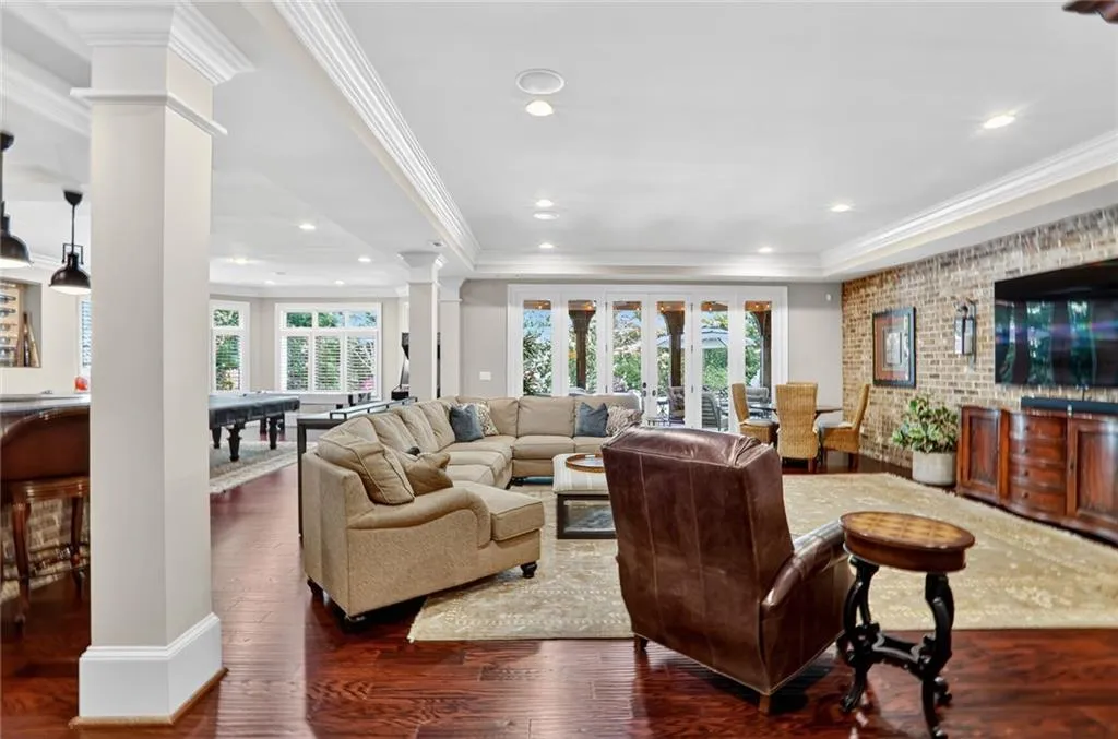 Living area featuring dark wood finished floors, a raised ceiling, decorative columns, ornamental molding, and brick wall