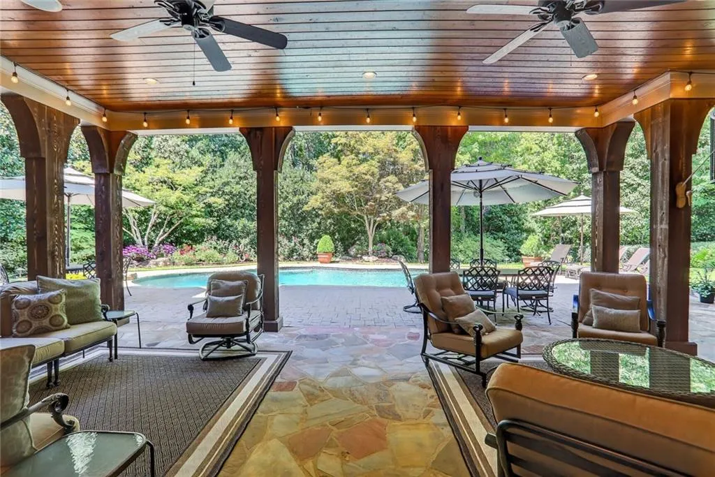 View of patio featuring an outdoor pool, a ceiling fan, and view of wooded area
