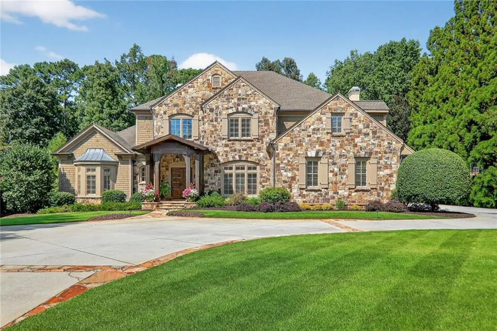 View of front facade featuring a front yard, a chimney, stone siding, roof with shingles, and concrete driveway