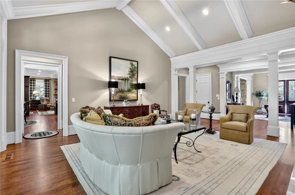 Living room with ornate columns, wood finished floors, beam ceiling, high vaulted ceiling, and ornamental molding