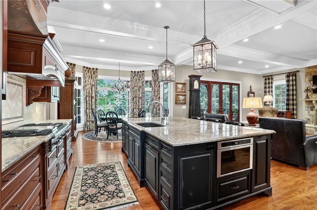 Kitchen featuring dark cabinetry, light stone counters, light wood-style flooring, beam ceiling, and pendant lighting