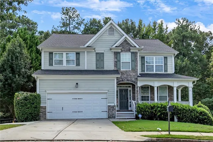 Two-story residence featuring a covered front porch, stone accents, two-car garage, and established landscaping