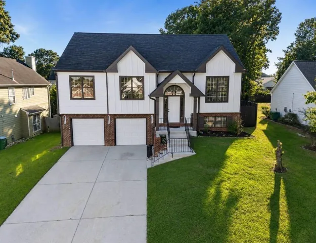 Contemporary split-level exterior with a dark shingled roof, white siding, and brick accents