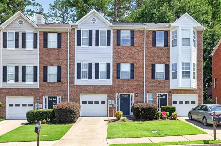 Brick and siding townhouse exterior featuring three levels, multiple windows with shutters, and attached garages